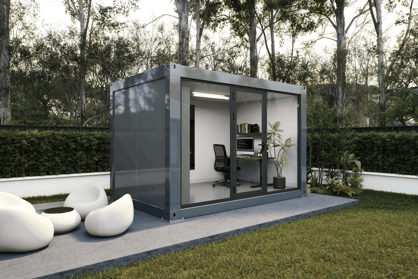 A modern modular office pod with a dark gray metal frame and glass sliding doors, situated on a concrete patio in a landscaped garden with green grass, hedges, and trees.
