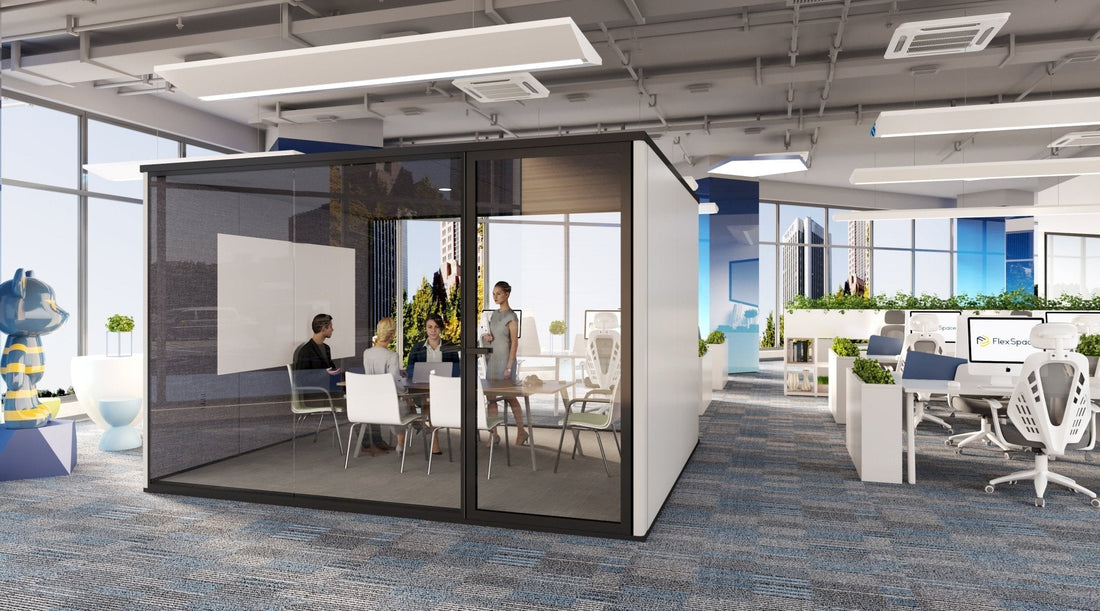 Modular office cube with black trim and people around a desk in a large open plan office