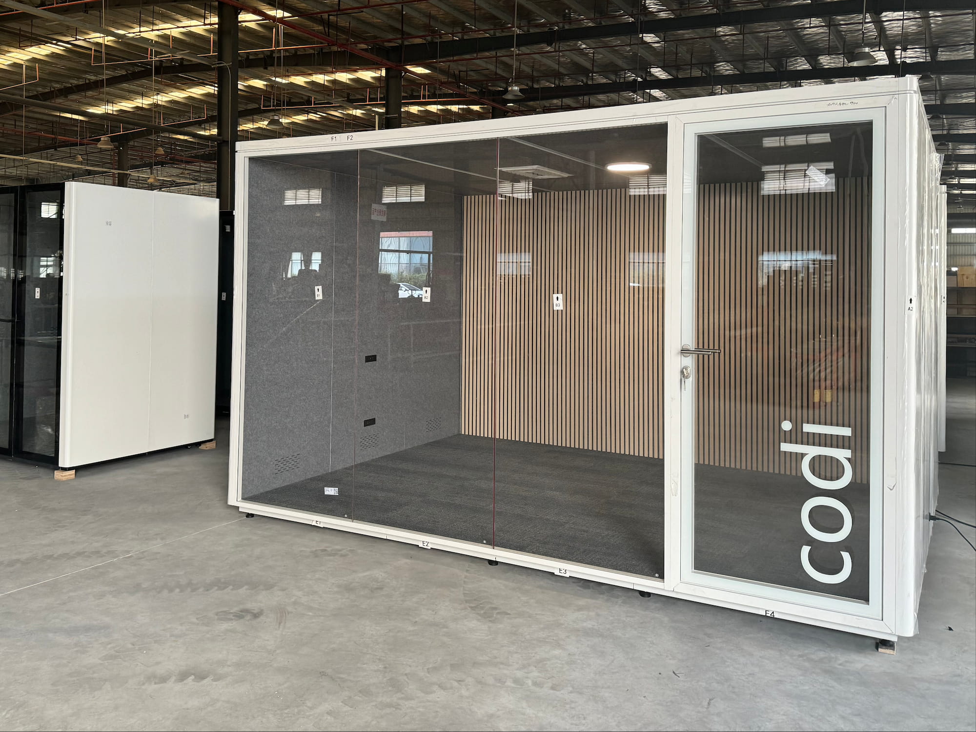 Modular office pod with glass walls and 'codi' branding in a warehouse setting.