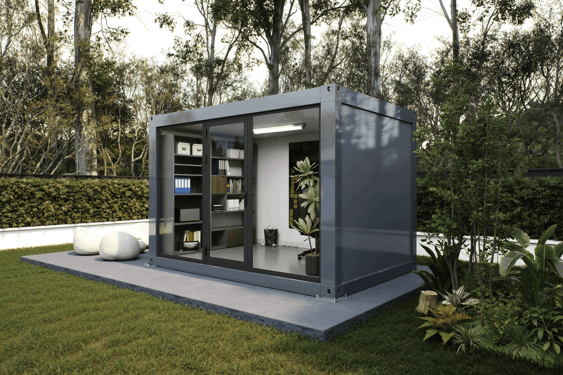 A modern gray modular outdoor office pod with large glass windows, shown on a concrete platform in a landscaped garden with trees and grass.