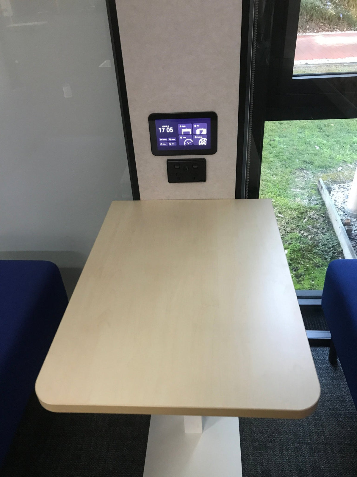inside an office pod with blond wood table and digital controls and blue seats