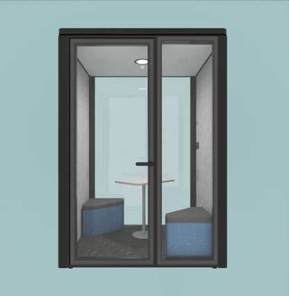 A modern glass meeting pod enclosure with a dark charcoal frame, featuring a built-in table and two blue upholstered bench seats inside, shown against a solid light blue background.