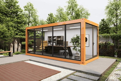 A modern modular office pod with a bright orange-brown frame and large glass windows, situated on a concrete patio in a landscaped garden setting.