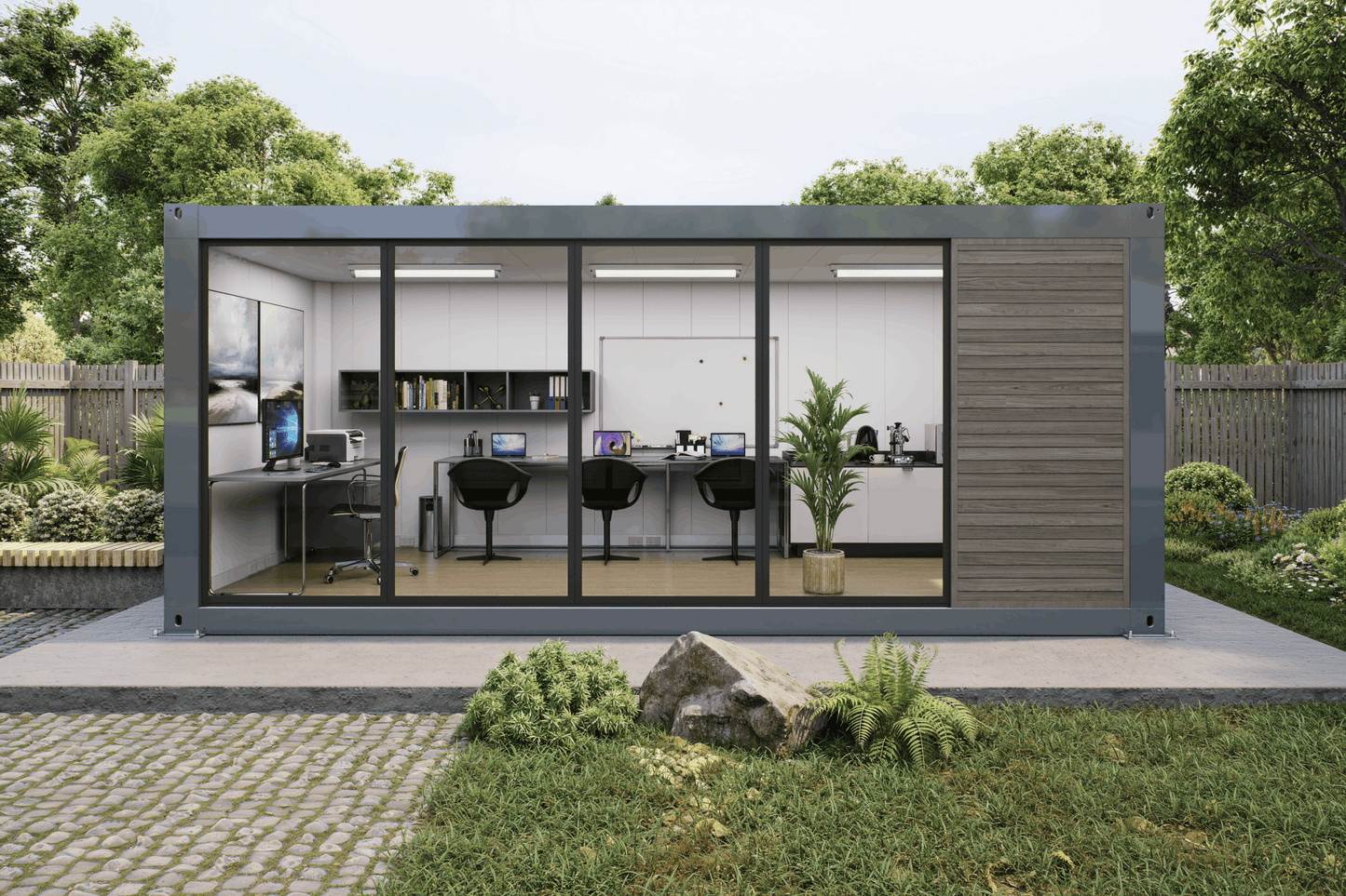 A modern modular office pod with large glass windows and a dark gray metal frame, set on a concrete patio in a landscaped garden with trees and grass.