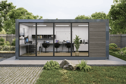 A modern modular office pod with large glass windows and a dark gray metal frame, set on a concrete patio in a landscaped garden with trees and grass.